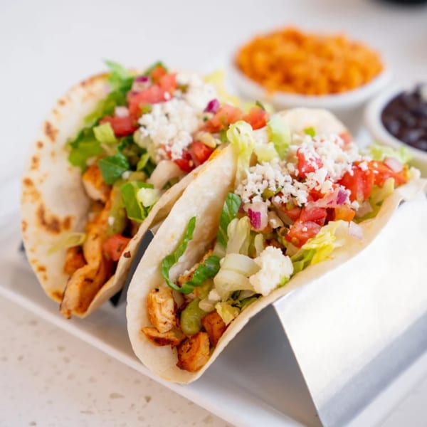 Two chicken tacos with lettuce, tomato, onion, and cheese, with sides of rice and beans.