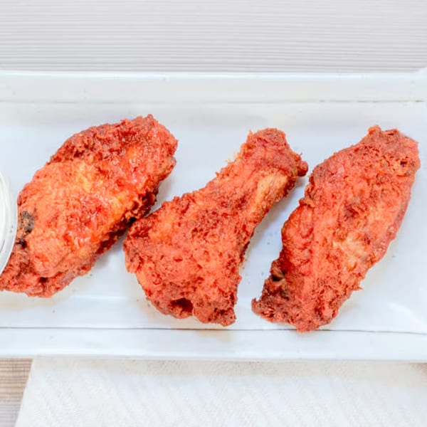 Three crispy, red-orange fried chicken wings on a white rectangular plate, with a small white dipping sauce cup.