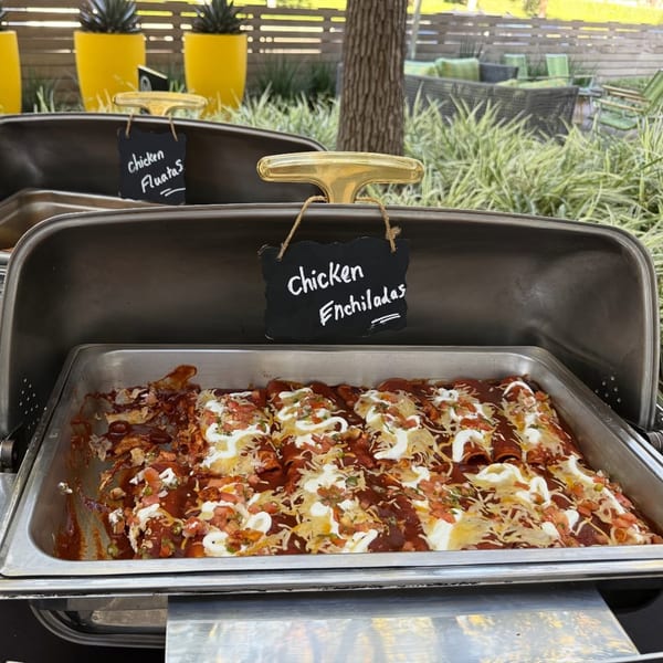 A catering tray of chicken enchiladas with red sauce, cheese, sour cream, and pico de gallo.