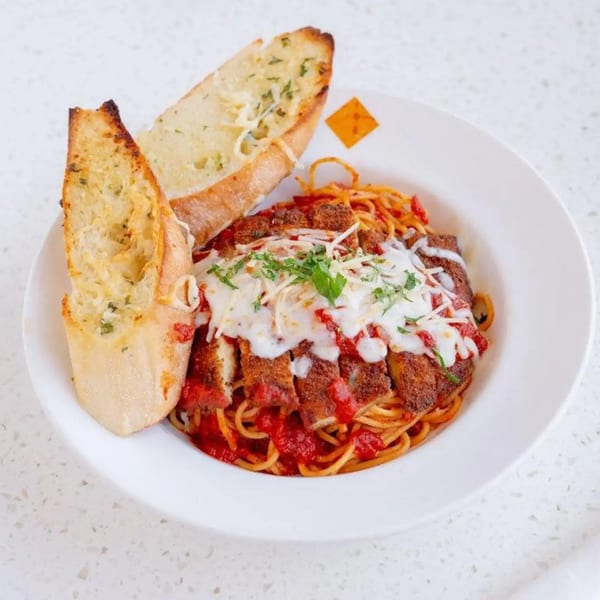 Chicken parmesan with spaghetti and red sauce, topped with melted cheese and parsley, served with garlic bread.
