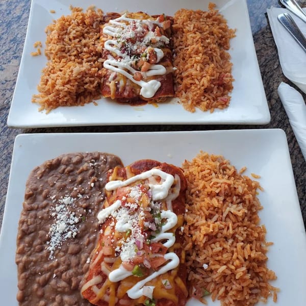 Two plates of enchiladas with rice, one also with refried beans, topped with sour cream and pico de gallo.