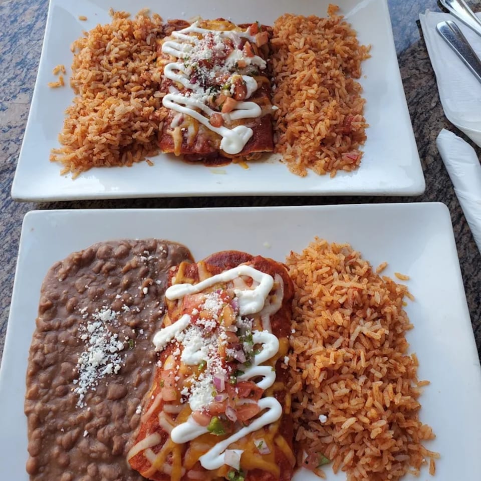 Two plates of enchiladas with rice, one also with refried beans, topped with sour cream and pico de gallo.