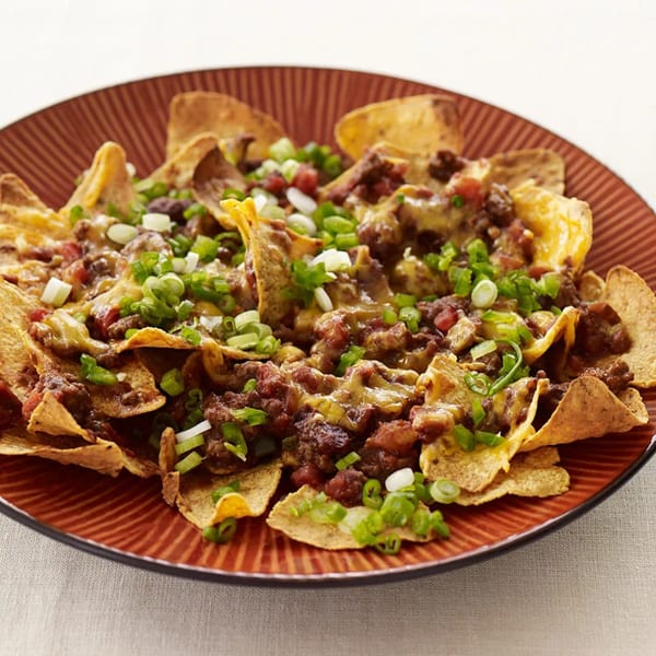 A plate of nachos with melted cheese, ground meat, diced tomatoes, and green onions.