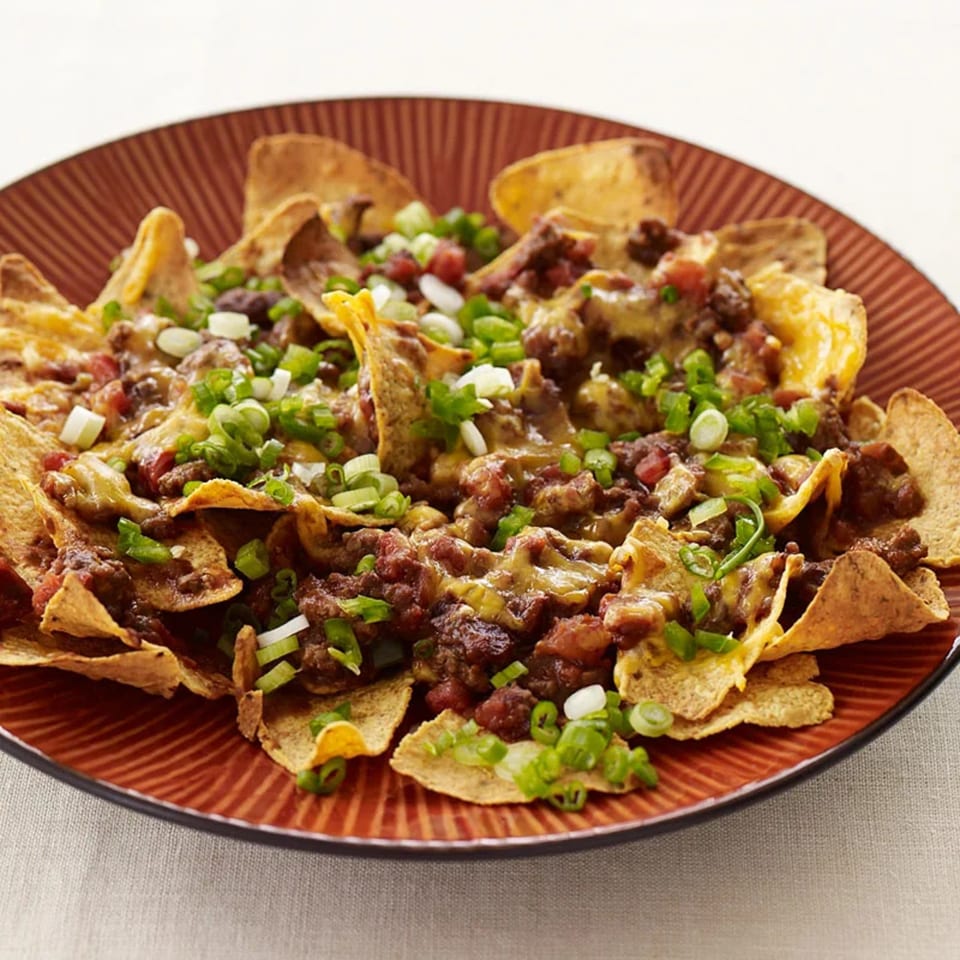 A plate of nachos with melted cheese, ground meat, diced tomatoes, and green onions.